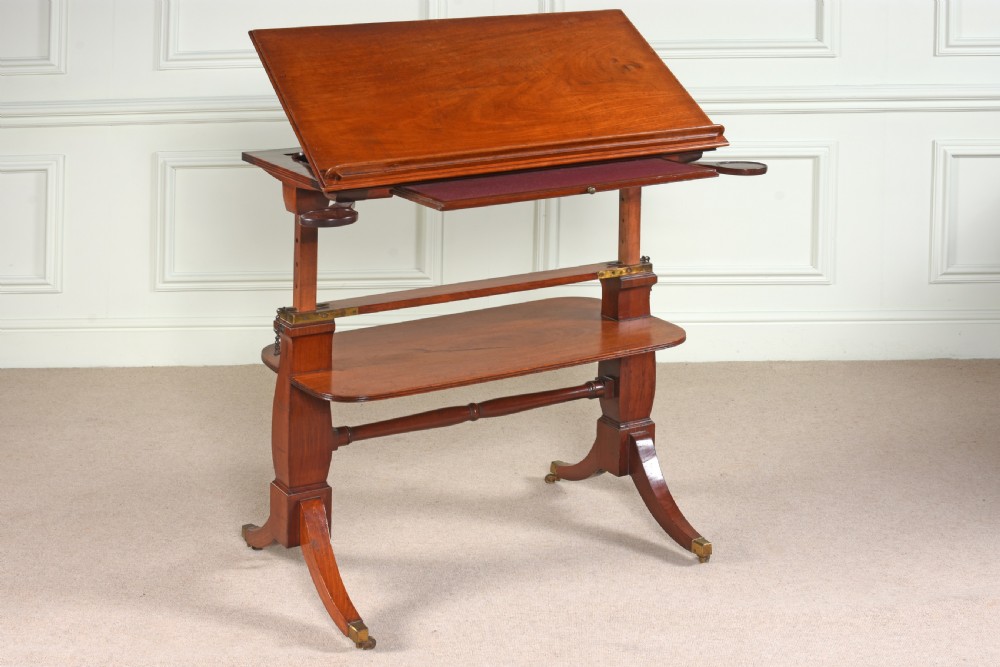 A George III mahogany architects table featuring an adjustable height mechanism, tilting top slope with book ledge, lower tier shelf, and splayed legs on brass castors. View II