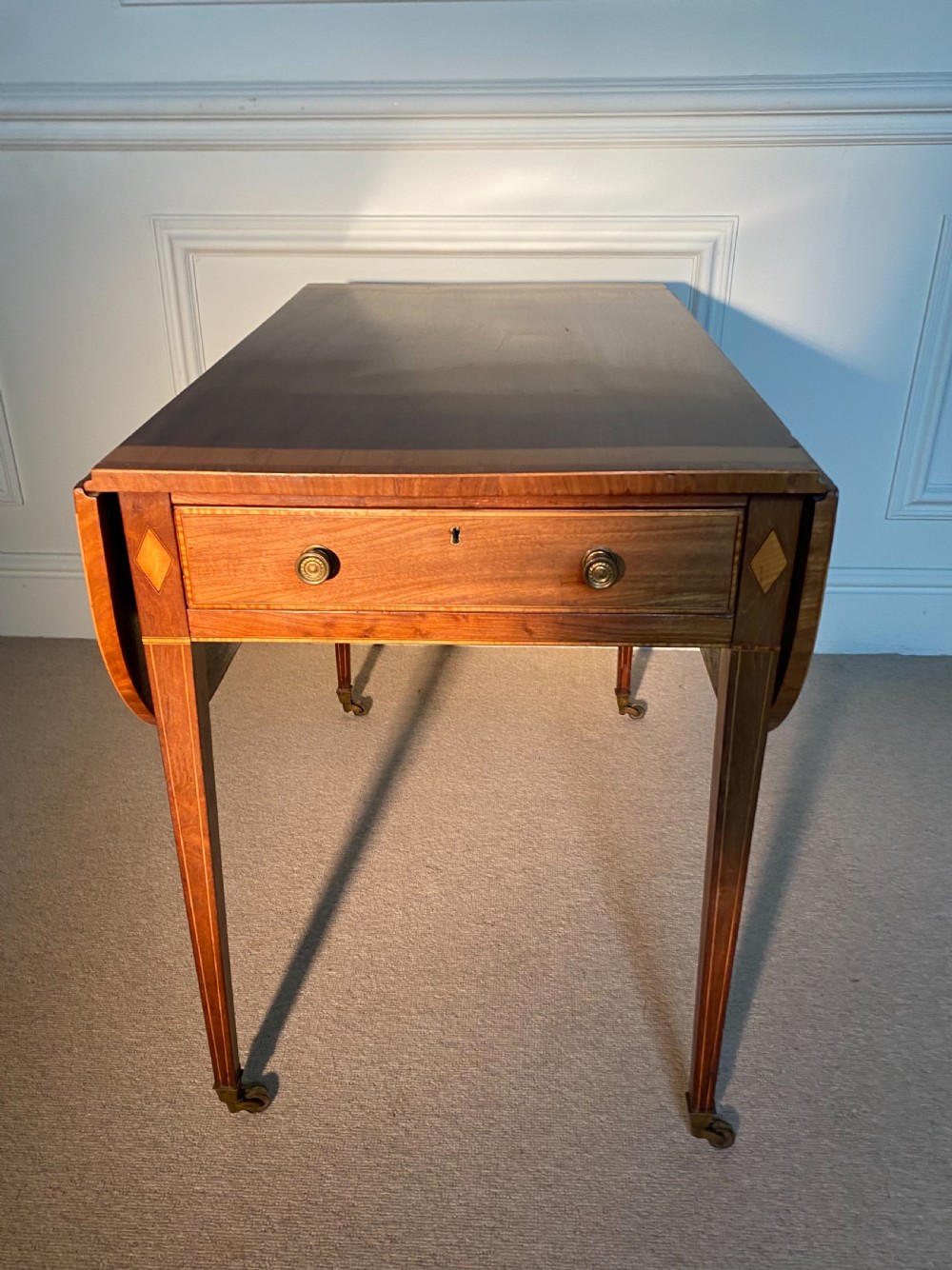 An 18th-century Sheraton mahogany Pembroke table featuring drop leaves, stringing inlay, a single drawer with brass knobs, and square tapered legs on brass castors. View II
