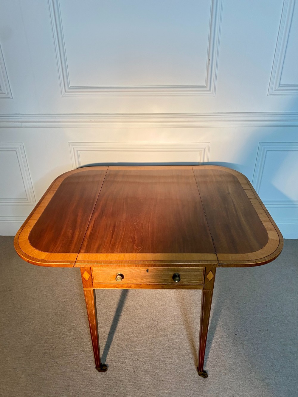 An 18th-century Sheraton mahogany Pembroke table featuring drop leaves, stringing inlay, a single drawer with brass knobs, and square tapered legs on brass castors. View VIII