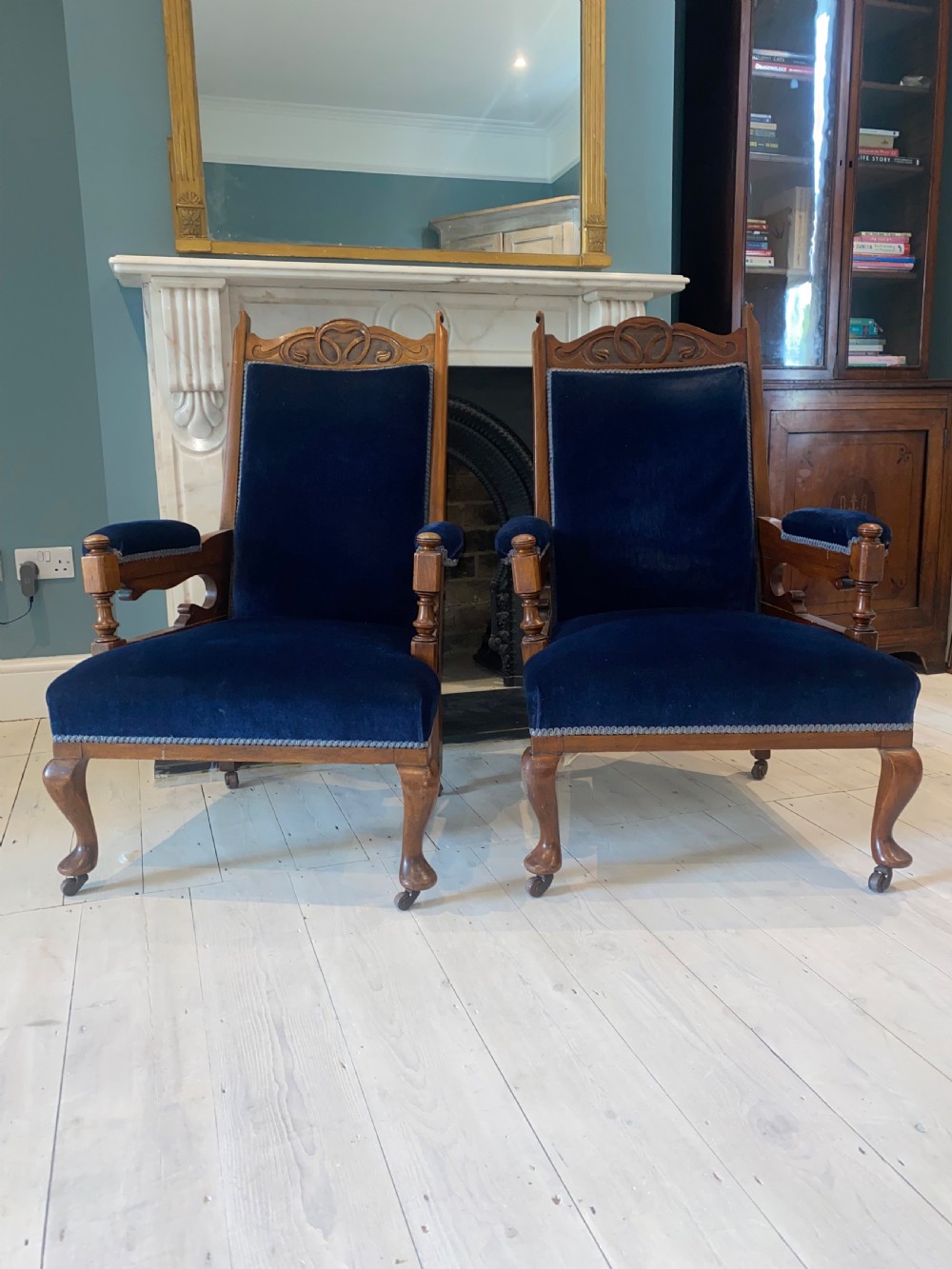 A pair of 19th-century walnut armchairs featuring carved crest rails, padded armrests, brass castors, and deep navy blue velvet upholstery. View II