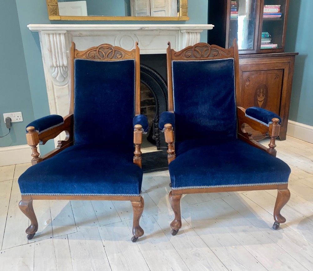A pair of 19th-century walnut armchairs featuring carved crest rails, padded armrests, brass castors, and deep navy blue velvet upholstery. View III