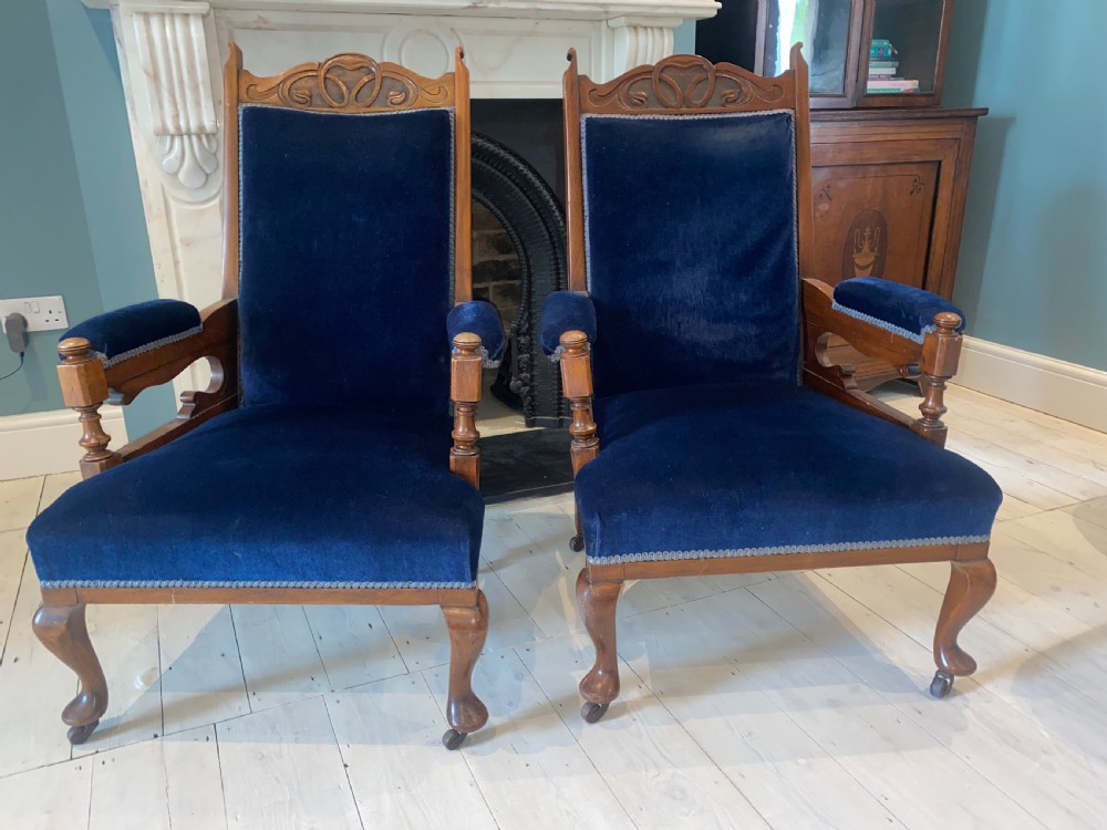 A pair of 19th-century walnut armchairs featuring carved crest rails, padded armrests, brass castors, and deep navy blue velvet upholstery. View V