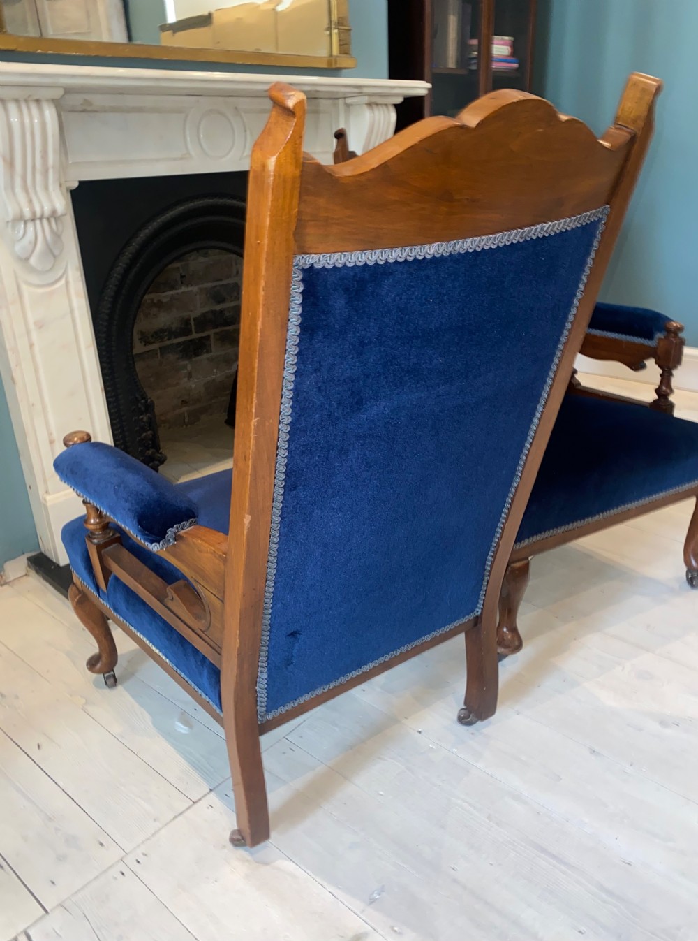 A pair of 19th-century walnut armchairs featuring carved crest rails, padded armrests, brass castors, and deep navy blue velvet upholstery. View X