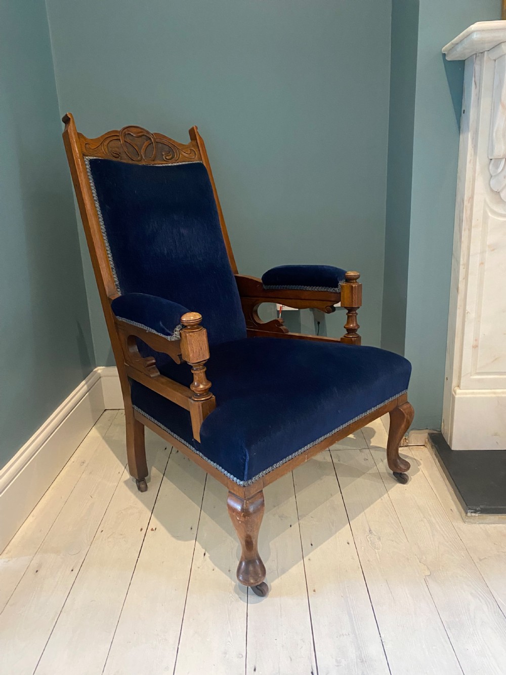 A pair of 19th-century walnut armchairs featuring carved crest rails, padded armrests, brass castors, and deep navy blue velvet upholstery. View XII