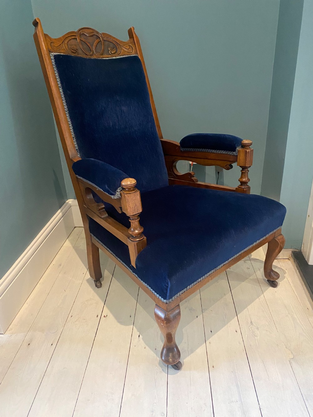 A pair of 19th-century walnut armchairs featuring carved crest rails, padded armrests, brass castors, and deep navy blue velvet upholstery. View XIV