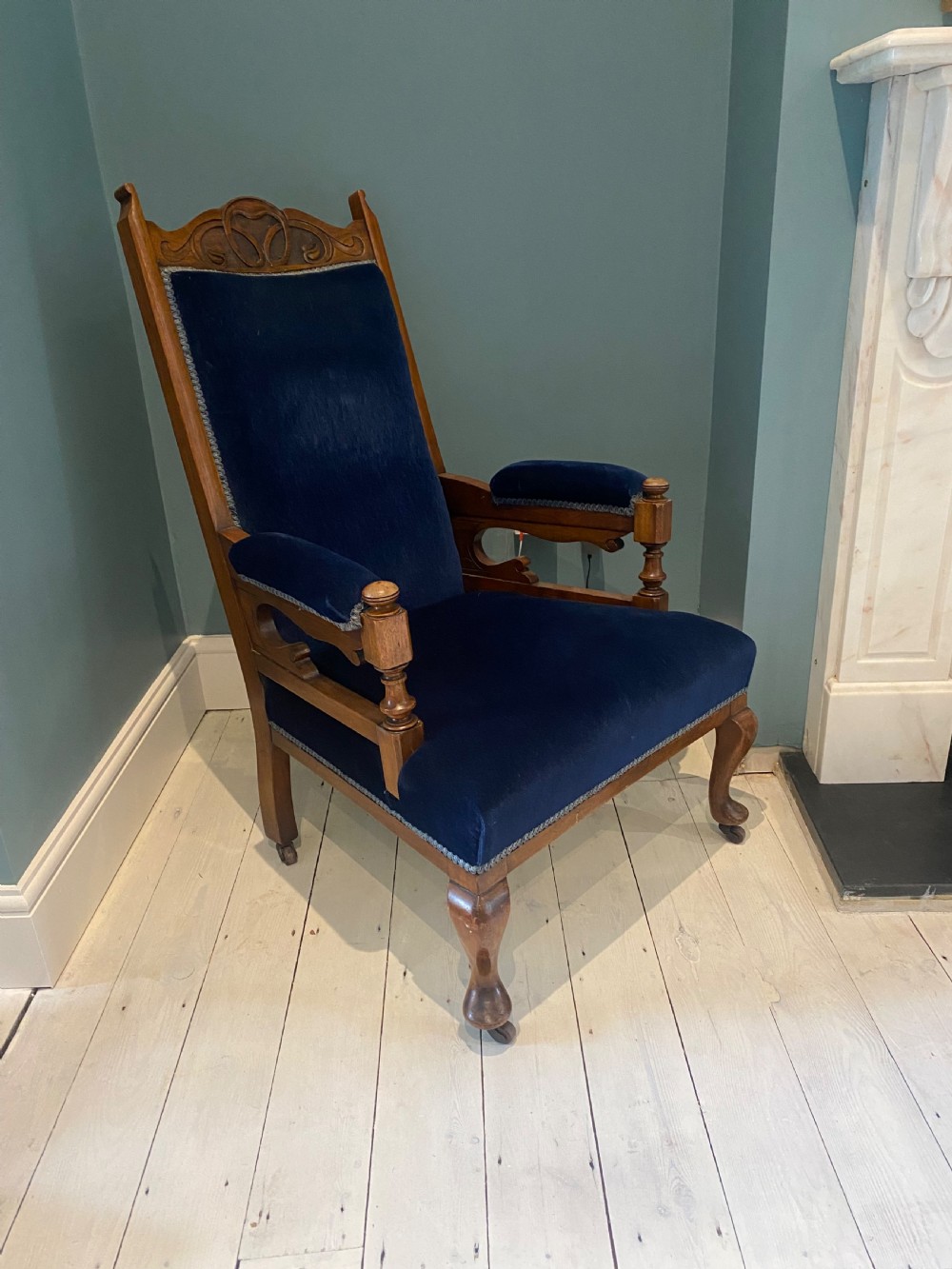 A pair of 19th-century walnut armchairs featuring carved crest rails, padded armrests, brass castors, and deep navy blue velvet upholstery. View XV