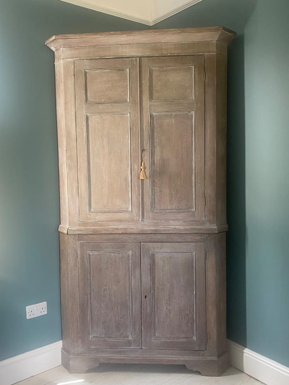 An 18th-century two-tier limed oak corner cupboard featuring raised panel doors, a moulded cornice, and a plinth base.