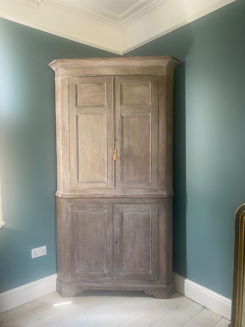 An 18th-century two-tier limed oak corner cupboard featuring raised panel doors, a moulded cornice, and a plinth base. View II
