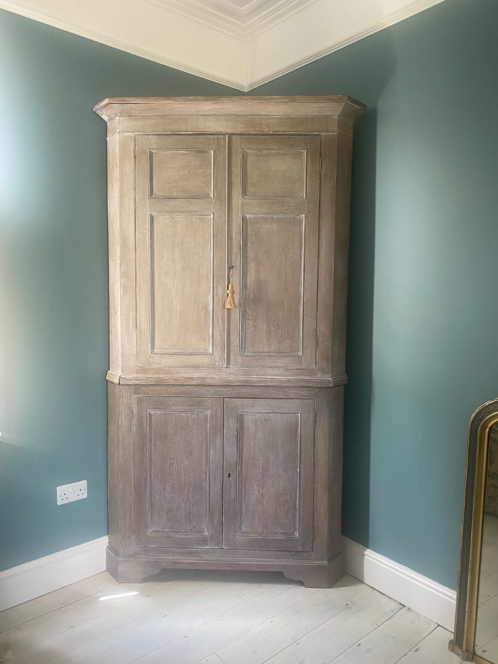 An 18th-century two-tier limed oak corner cupboard featuring raised panel doors, a moulded cornice, and a plinth base. View III