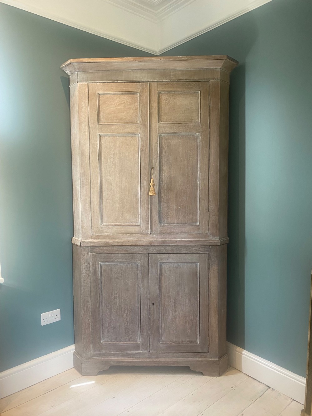 An 18th-century two-tier limed oak corner cupboard featuring raised panel doors, a moulded cornice, and a plinth base. View IV