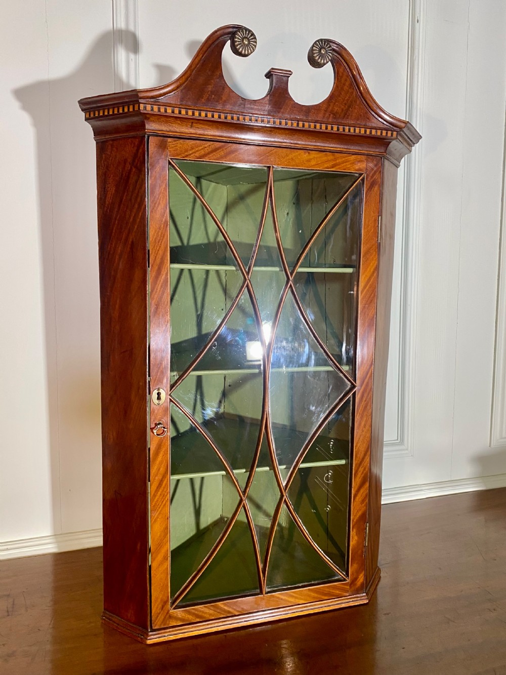 An eighteenth-century mahogany glazed corner cupboard with a swan neck pediment, carved rosettes, dentil inlay, and a green painted interior. View II