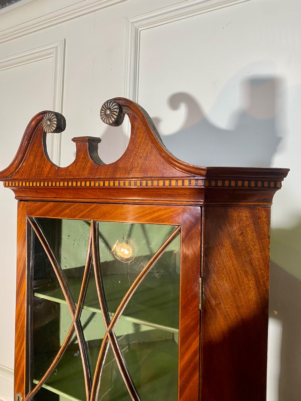 An eighteenth-century mahogany glazed corner cupboard with a swan neck pediment, carved rosettes, dentil inlay, and a green painted interior. View III