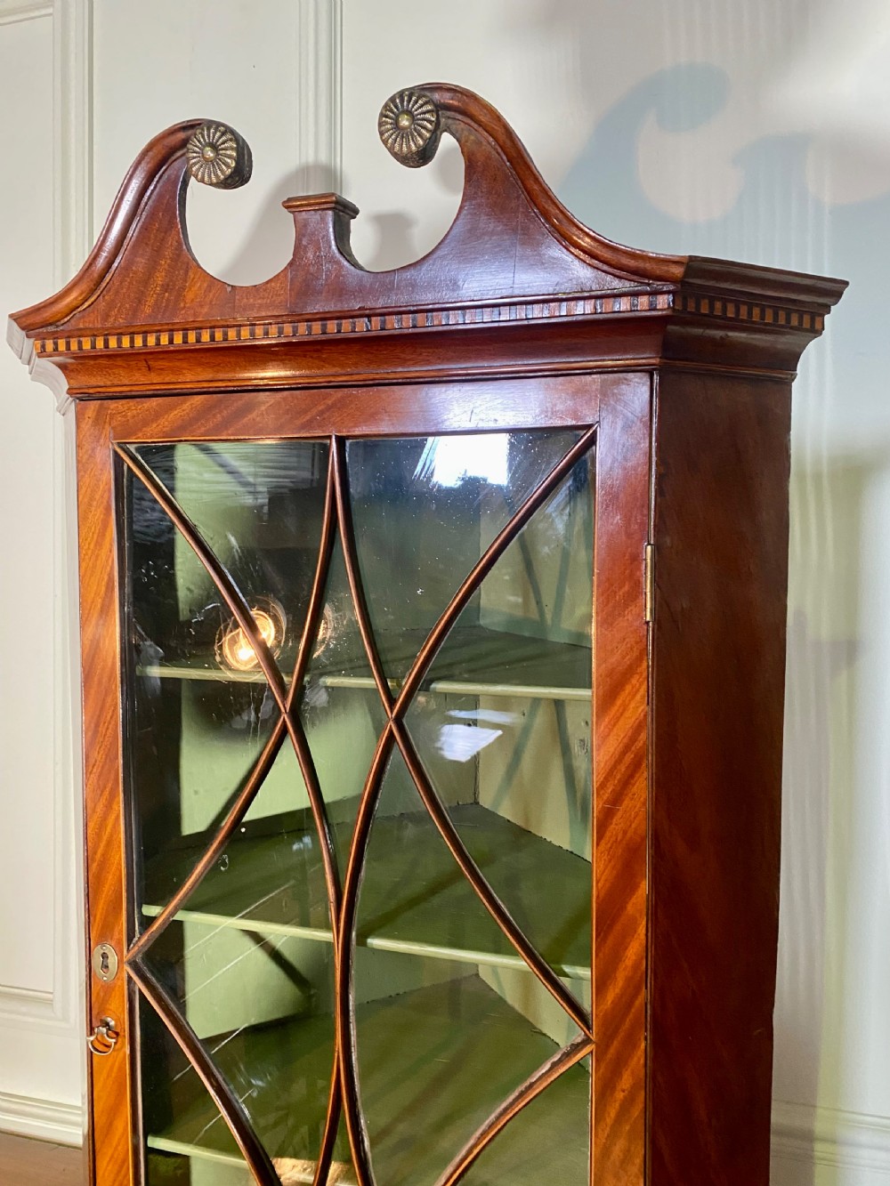 An eighteenth-century mahogany glazed corner cupboard with a swan neck pediment, carved rosettes, dentil inlay, and a green painted interior. View IV