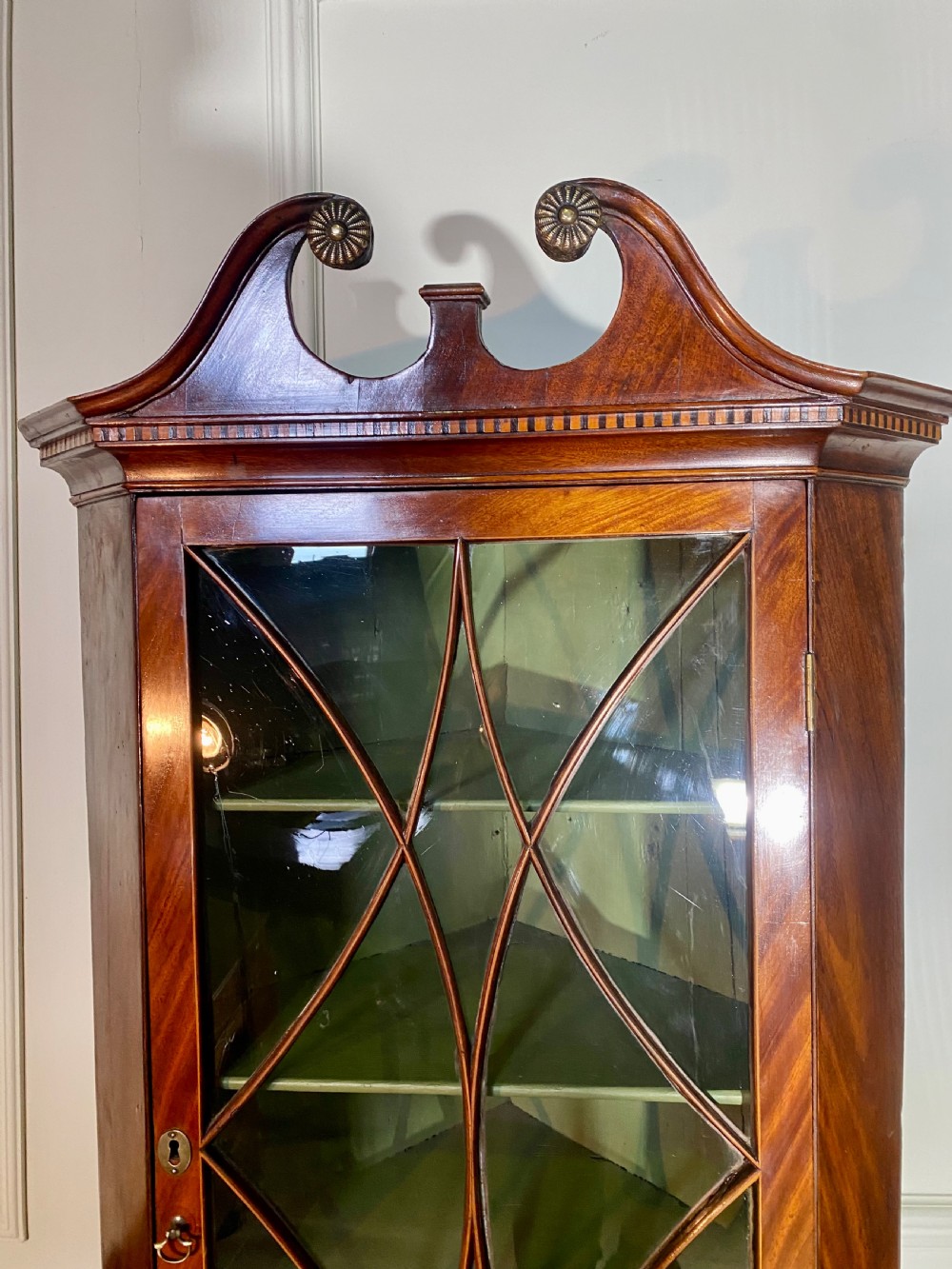 An eighteenth-century mahogany glazed corner cupboard with a swan neck pediment, carved rosettes, dentil inlay, and a green painted interior. View V