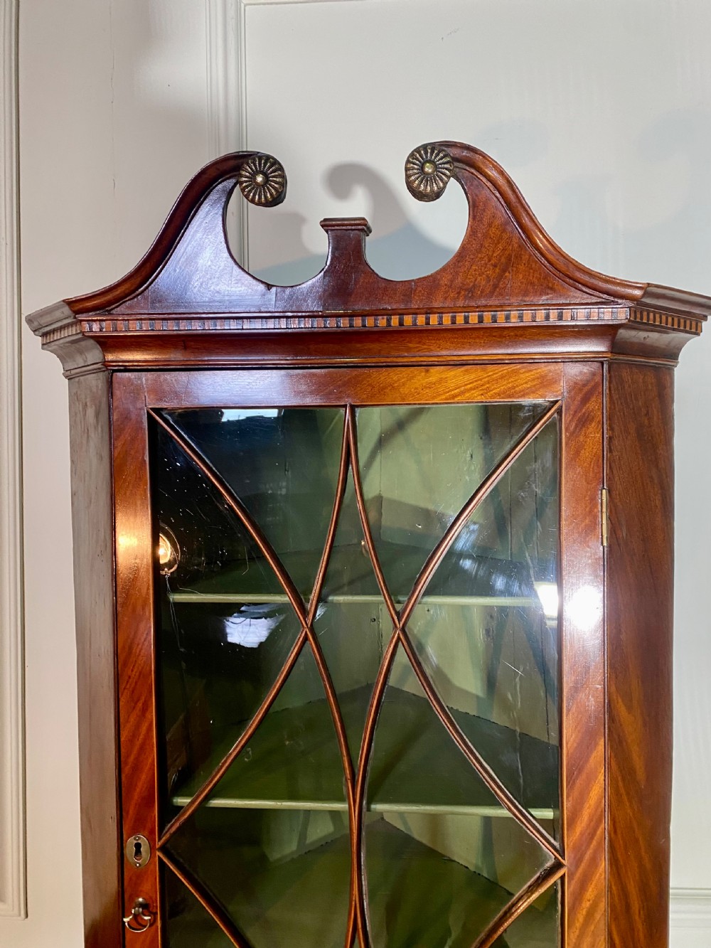 An eighteenth-century mahogany glazed corner cupboard with a swan neck pediment, carved rosettes, dentil inlay, and a green painted interior. View VI