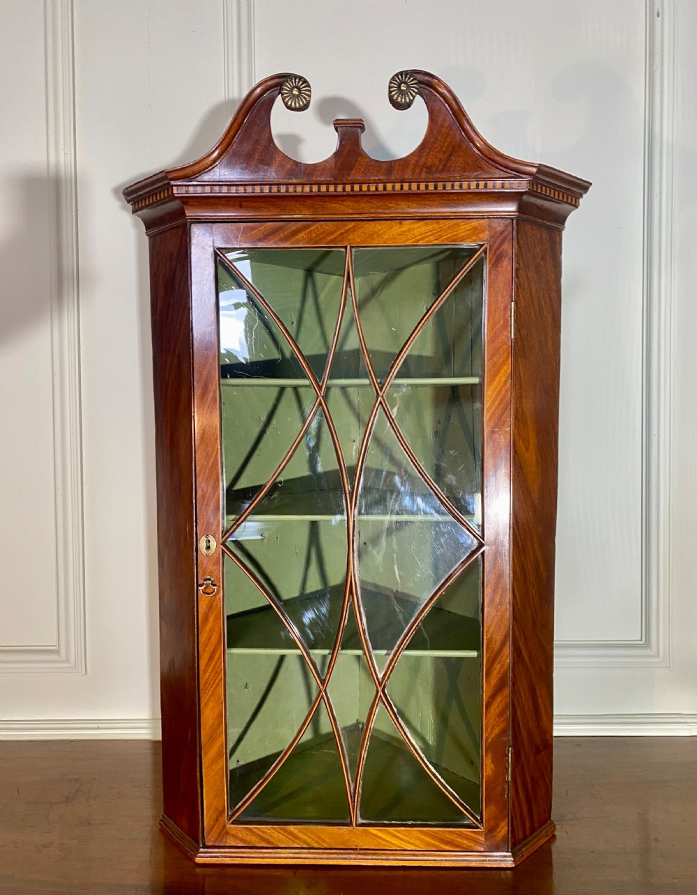An eighteenth-century mahogany glazed corner cupboard with a swan neck pediment, carved rosettes, dentil inlay, and a green painted interior. View VII