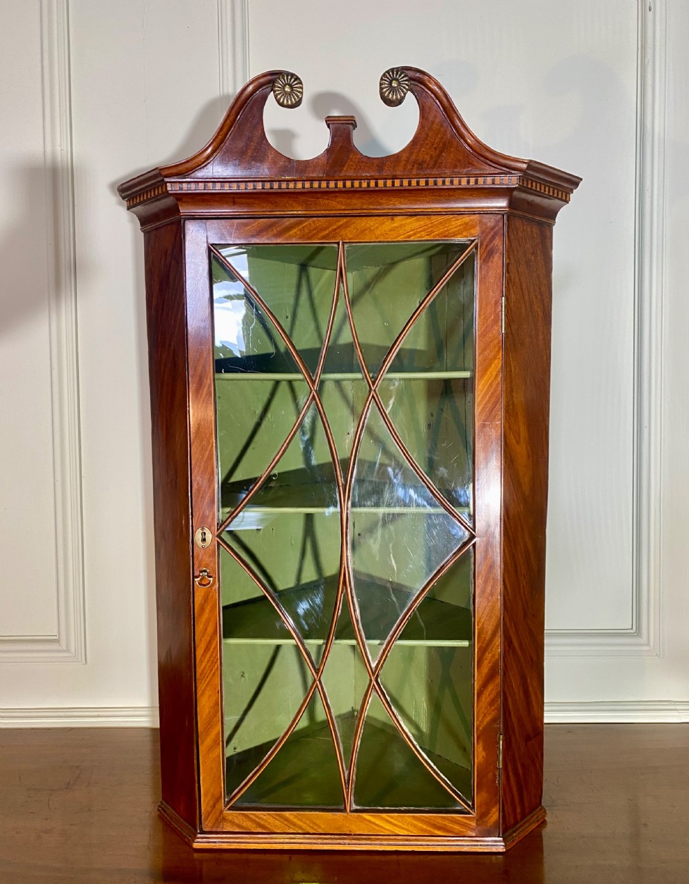 An eighteenth-century mahogany glazed corner cupboard with a swan neck pediment, carved rosettes, dentil inlay, and a green painted interior. View VIII