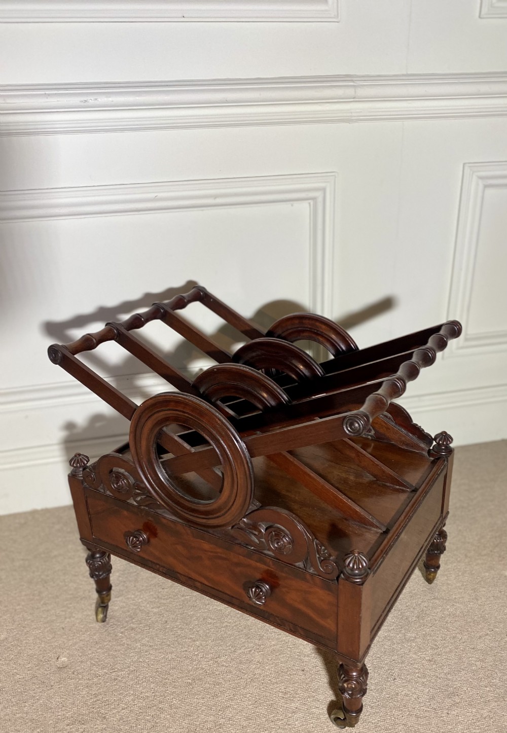 A Regency mahogany music canterbury featuring circular divided compartments, carved rosettes, a lower drawer with turned knobs, and carved legs on brass castors. View VIII