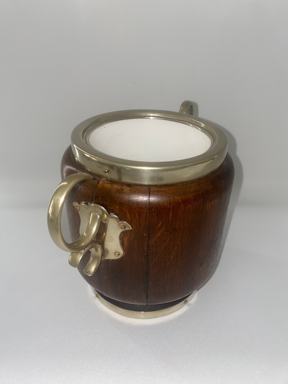 A turned oak ice bucket featuring silver-plated scroll handles, a shield-shaped front cartouche, and a domed metal lid with a finial. View VI
