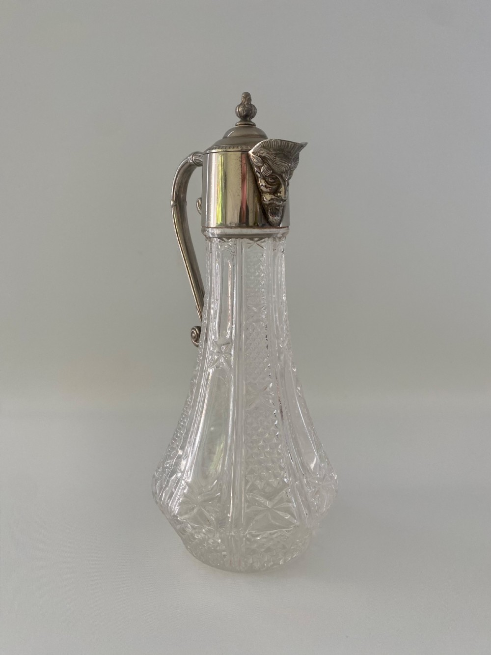 A cut crystal claret jug featuring a silver-plated collar, a mascaron face spout, and an ornate scroll handle. View III