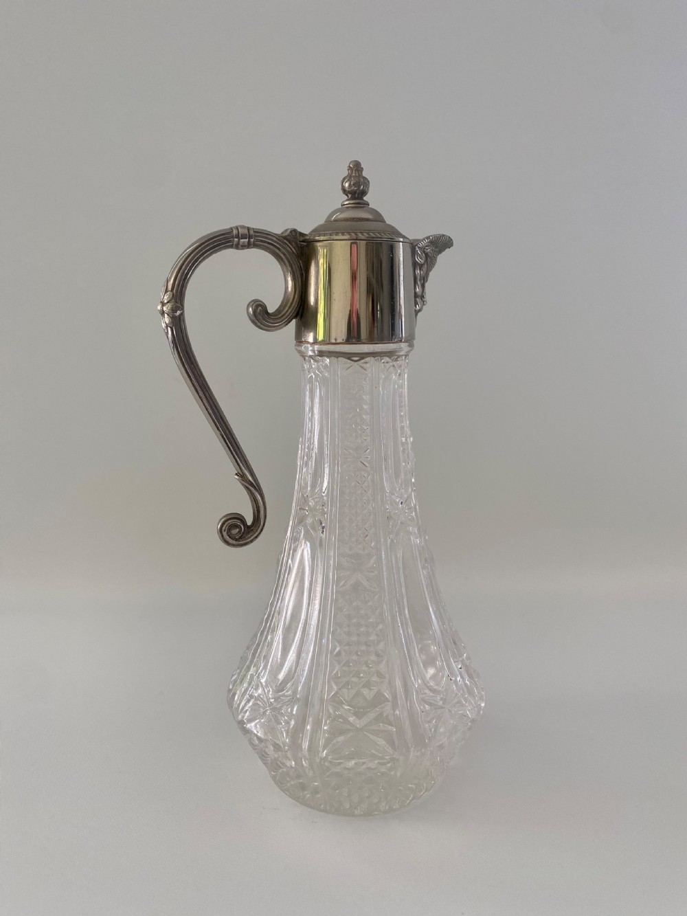A cut crystal claret jug featuring a silver-plated collar, a mascaron face spout, and an ornate scroll handle. View V