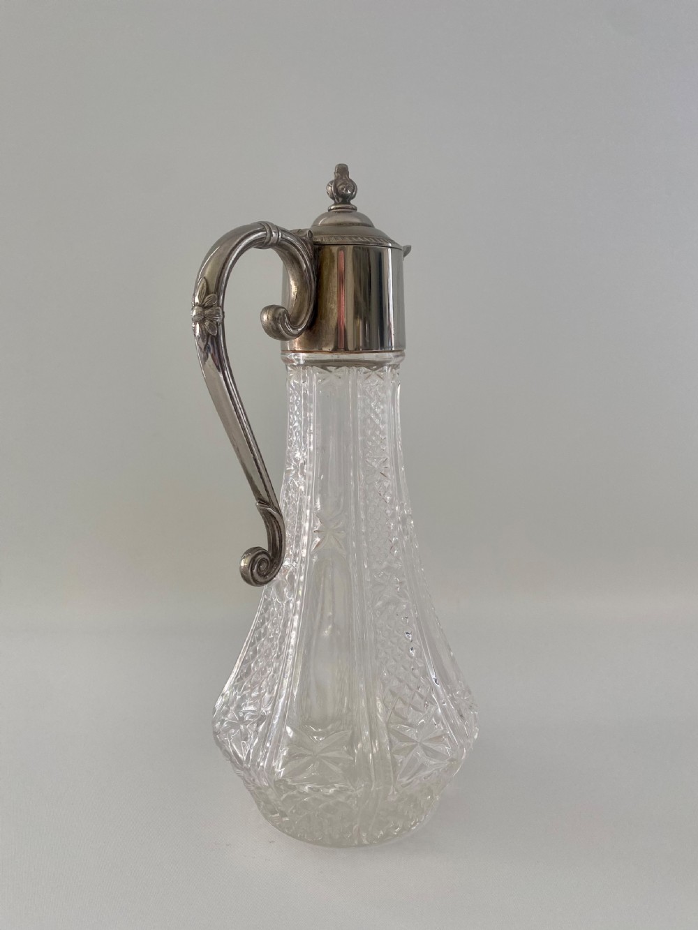 A cut crystal claret jug featuring a silver-plated collar, a mascaron face spout, and an ornate scroll handle. View VI