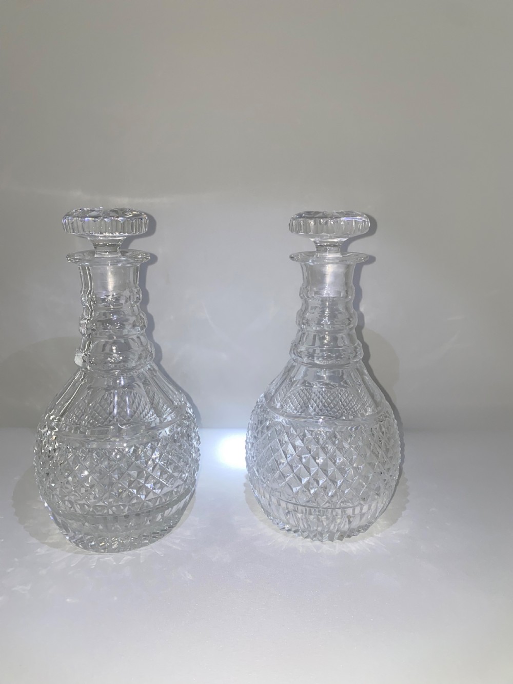 A pair of clear cut crystal glass decanters featuring diamond-cut lower bodies, ringed necks, and disc-shaped glass stoppers.
