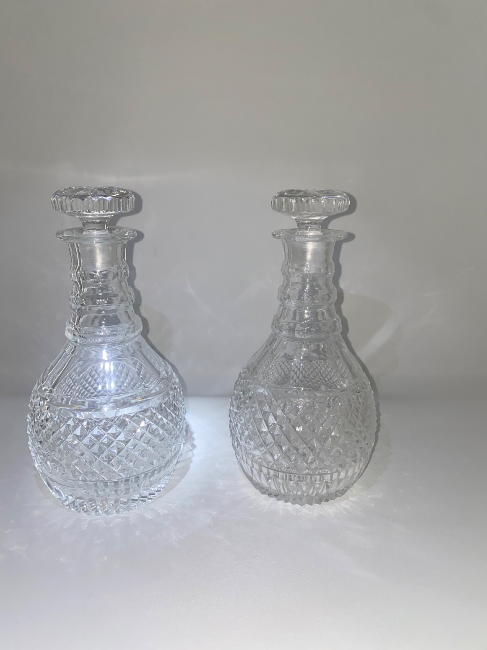 A pair of clear cut crystal glass decanters featuring diamond-cut lower bodies, ringed necks, and disc-shaped glass stoppers. View III