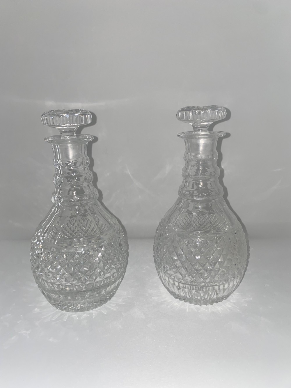 A pair of clear cut crystal glass decanters featuring diamond-cut lower bodies, ringed necks, and disc-shaped glass stoppers. View V