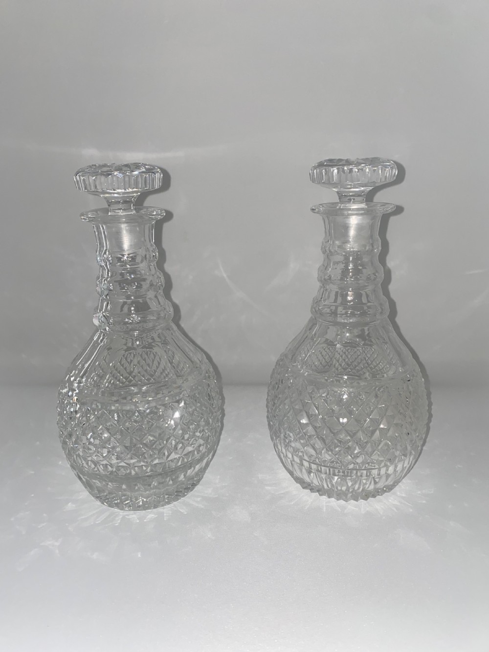 A pair of clear cut crystal glass decanters featuring diamond-cut lower bodies, ringed necks, and disc-shaped glass stoppers. View VI