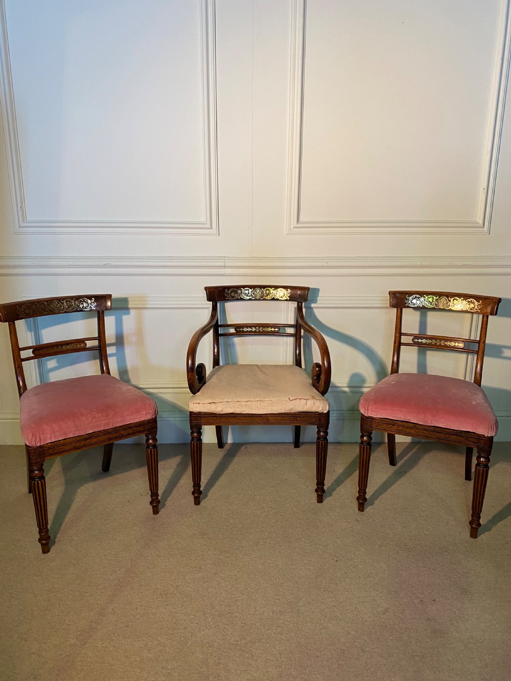 A set of Regency wooden dining chairs featuring brass inlay on the top rails, turned fluted legs, and upholstered drop-in seats.