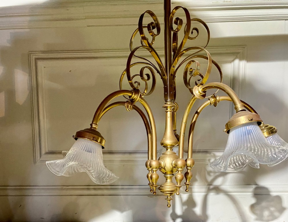 An Art Deco five-arm brass chandelier featuring scrolled upper accents and downward-facing ribbed frosted glass shades.