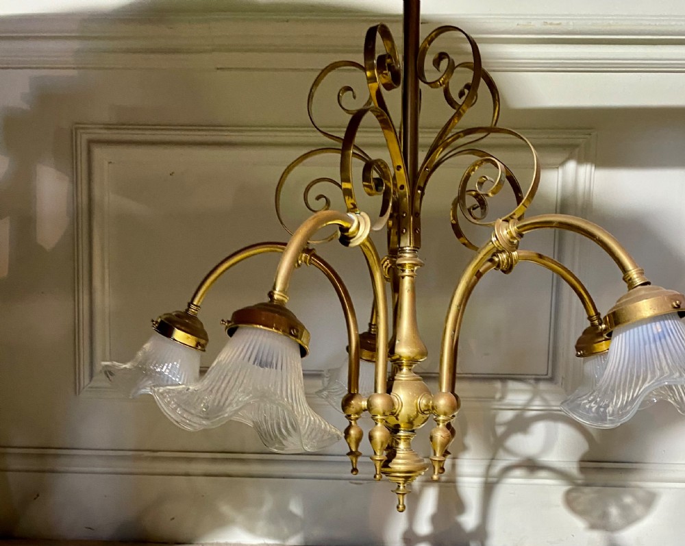 An Art Deco five-arm brass chandelier featuring scrolled upper accents and downward-facing ribbed frosted glass shades. View II