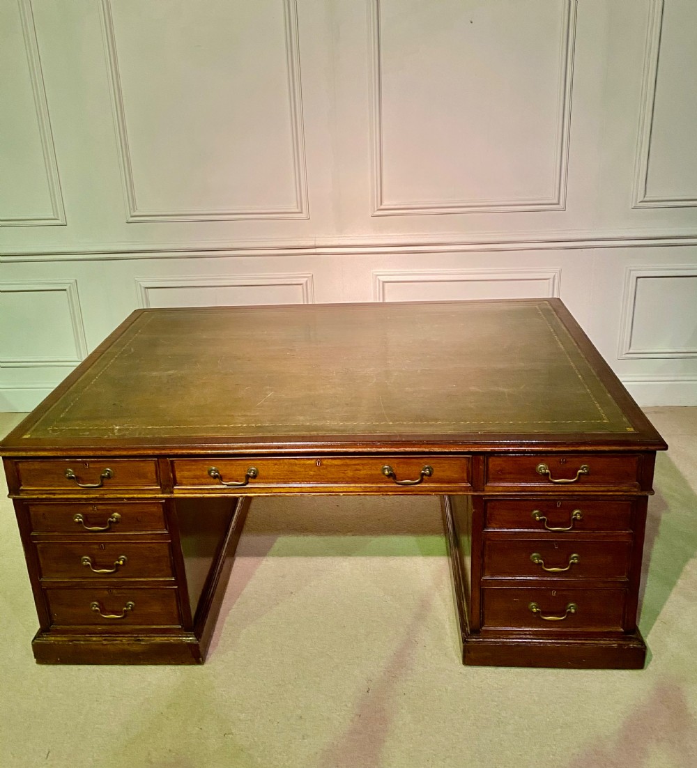 A nineteenth-century mahogany partners desk featuring a green leather inset writing surface, twin drawer pedestals, and brass drop handles.