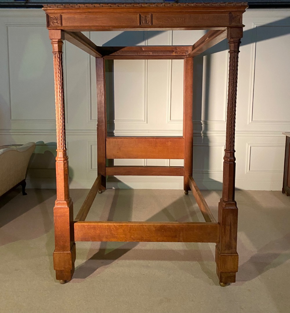An Arts and Crafts oak four poster bed frame featuring carved upright posts and a decorative upper frieze canopy structure.