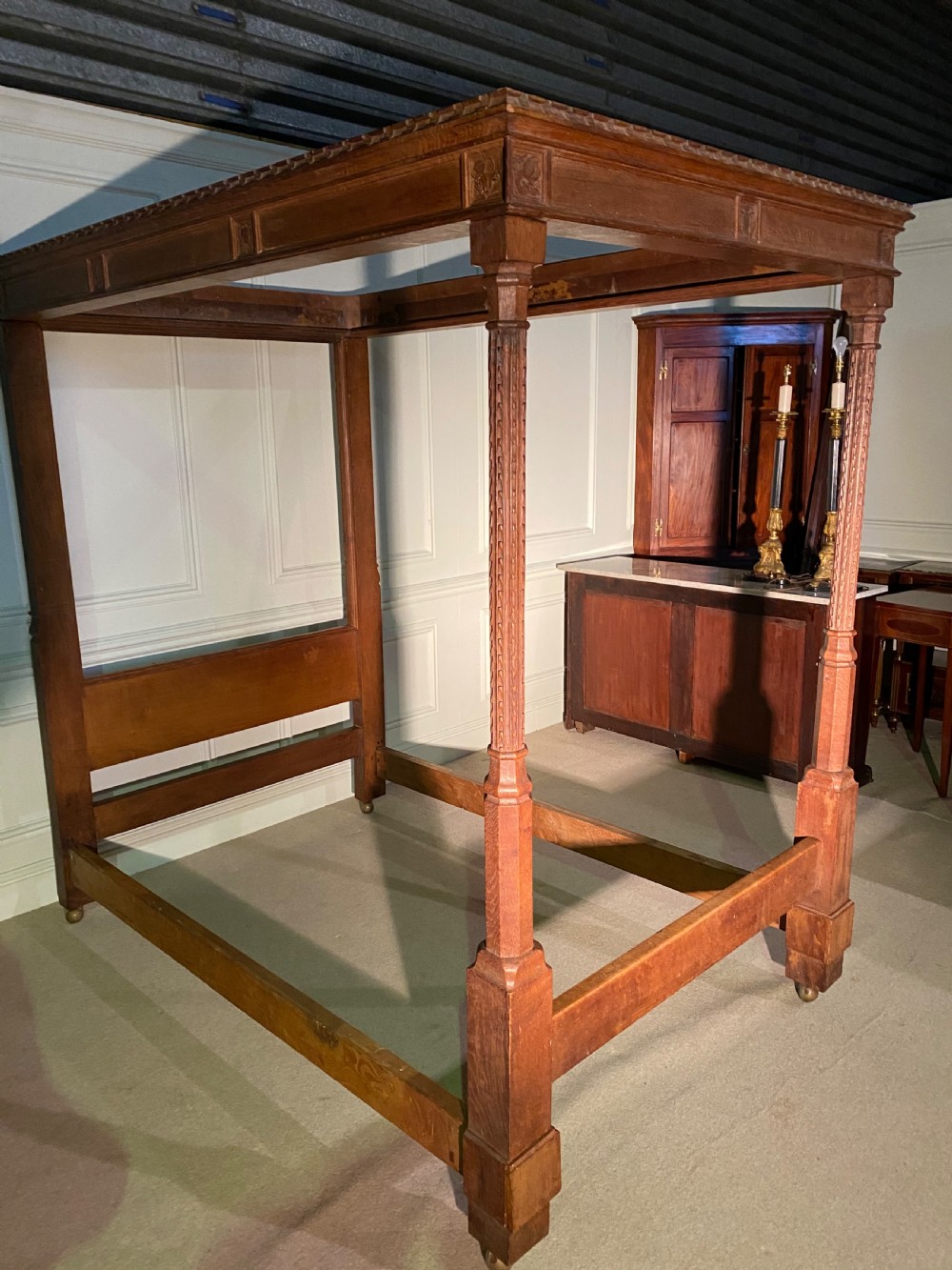 An Arts and Crafts oak four poster bed frame featuring carved upright posts and a decorative upper frieze canopy structure. View II