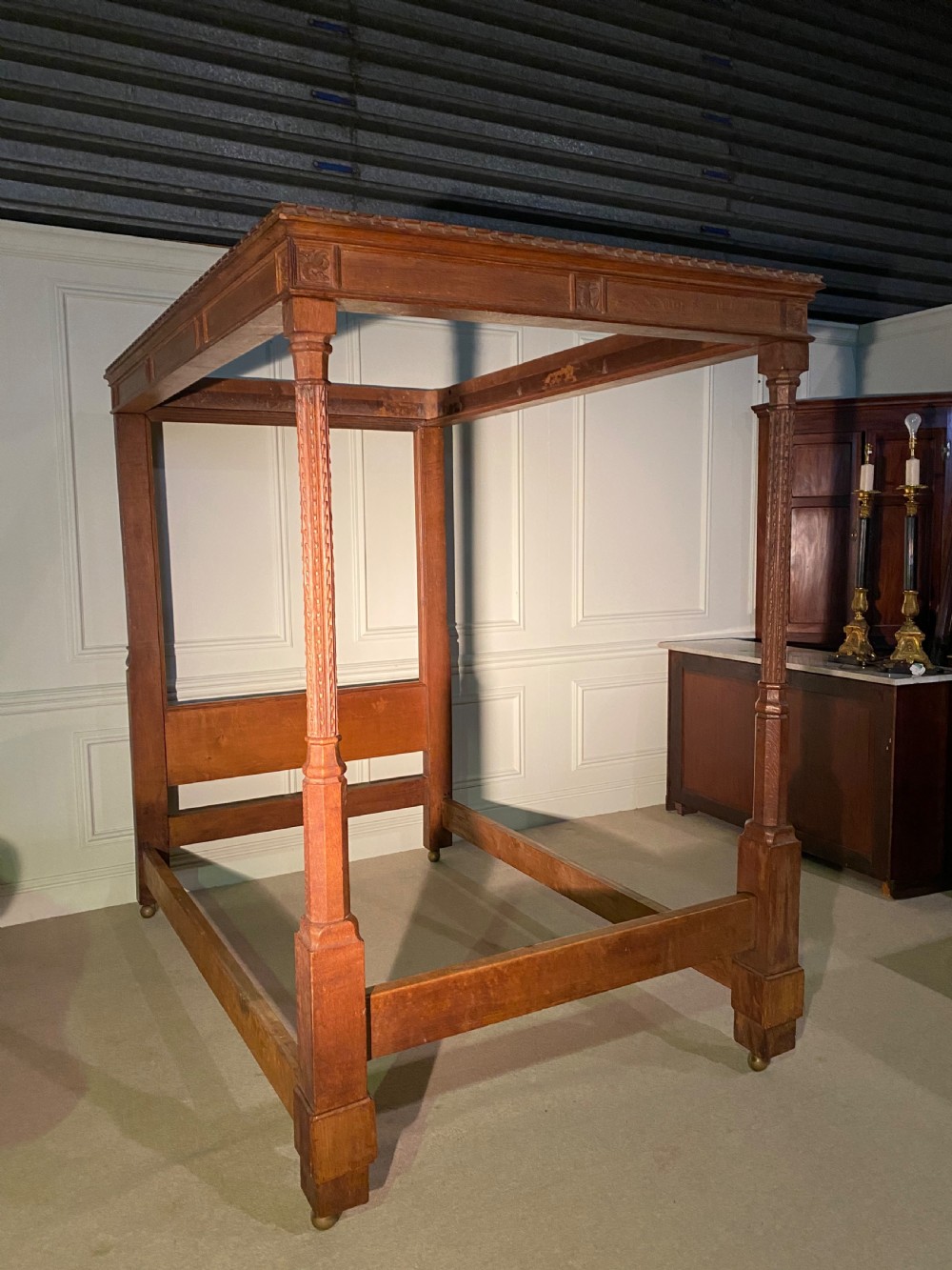 An Arts and Crafts oak four poster bed frame featuring carved upright posts and a decorative upper frieze canopy structure. View III