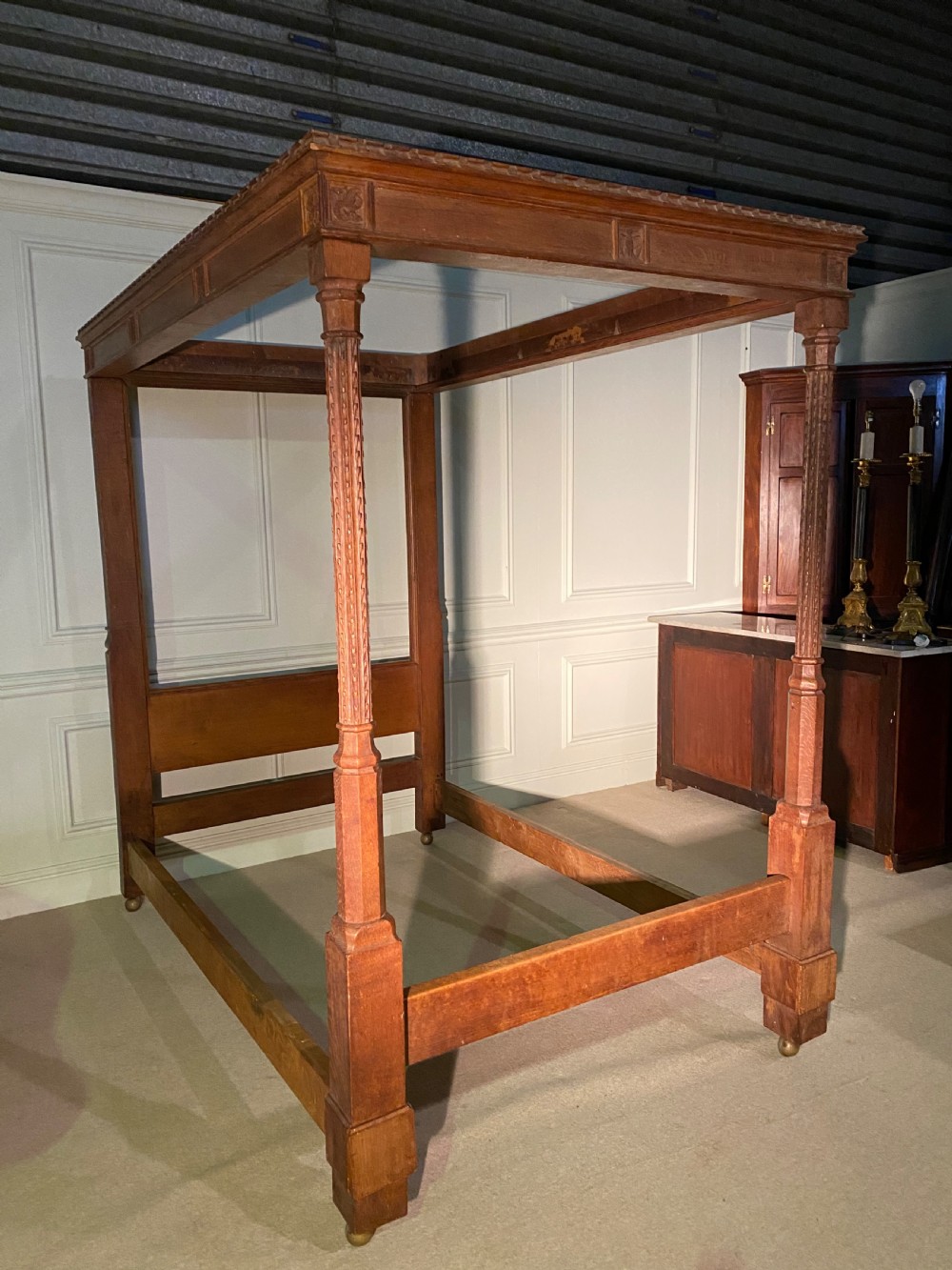 An Arts and Crafts oak four poster bed frame featuring carved upright posts and a decorative upper frieze canopy structure. View IV