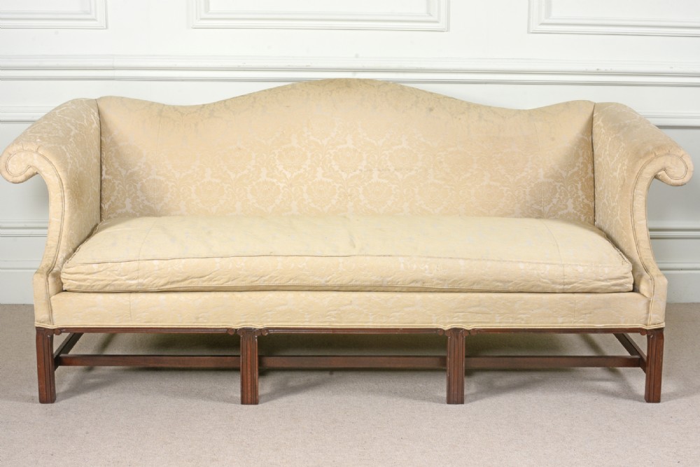 A George III style camel back sofa upholstered in pale cream damask fabric with six straight mahogany legs and stretchers.
