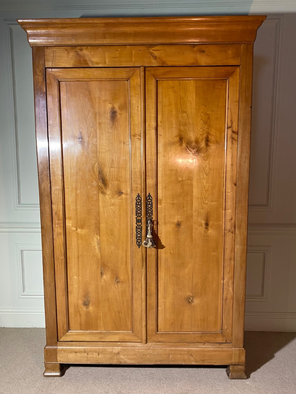 A tall 19th-century cherry wood armoire featuring double panelled doors, decorative iron keyplates, and a projecting upper cornice.