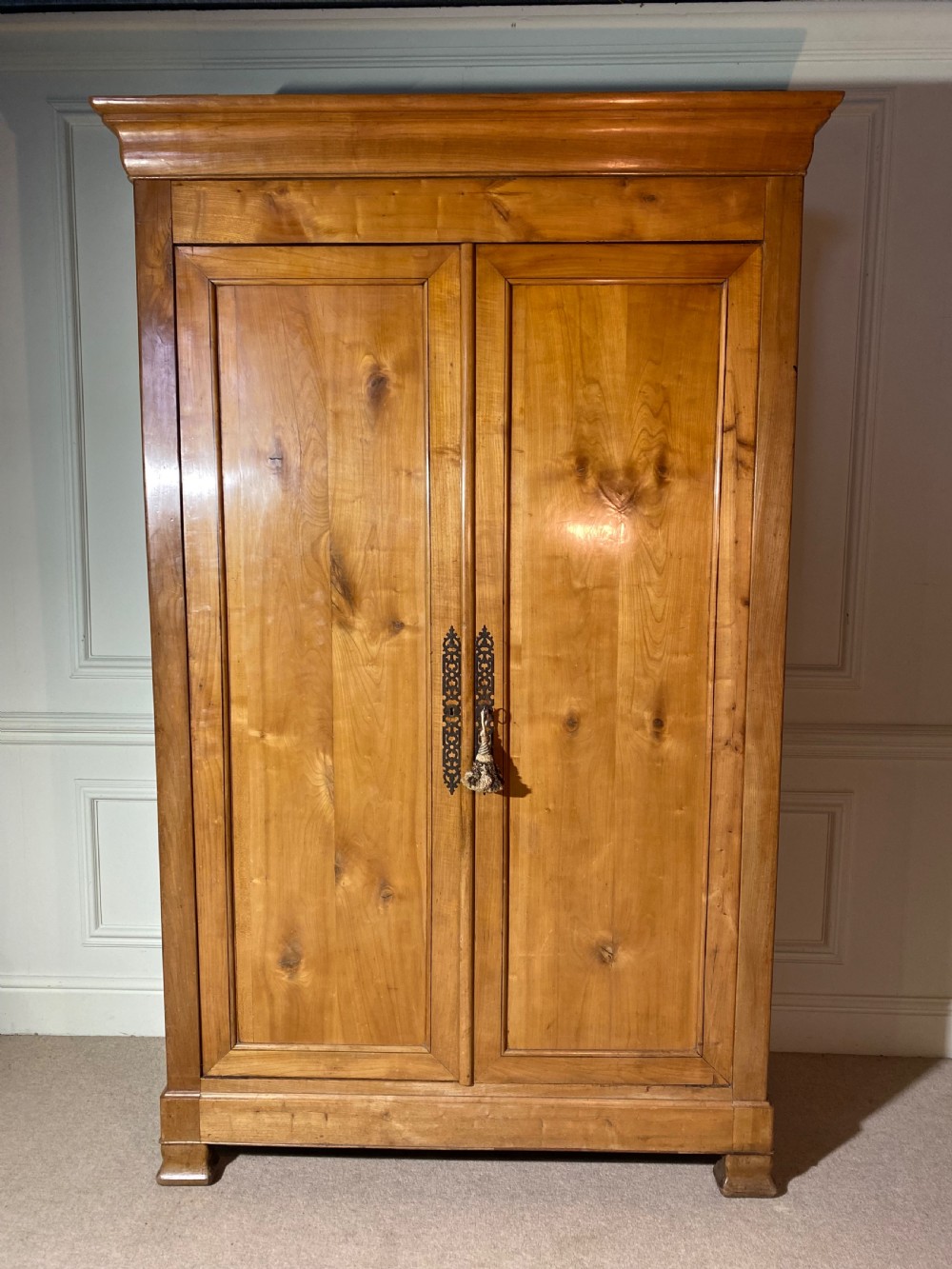 A tall 19th-century cherry wood armoire featuring double panelled doors, decorative iron keyplates, and a projecting upper cornice. View II