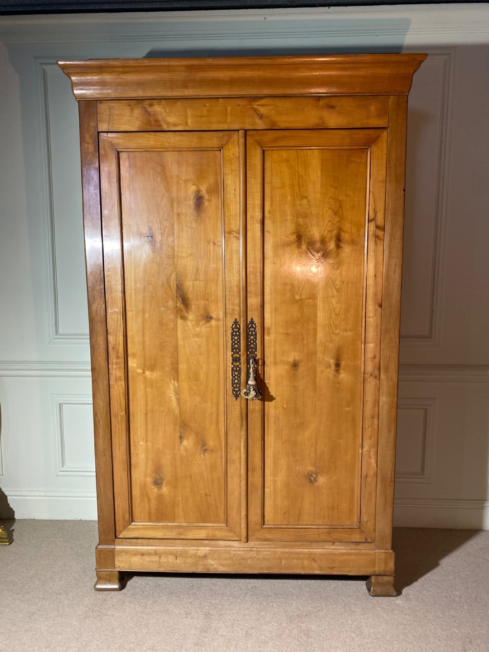 A tall 19th-century cherry wood armoire featuring double panelled doors, decorative iron keyplates, and a projecting upper cornice. View V