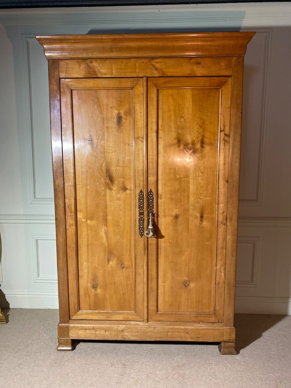 A tall 19th-century cherry wood armoire featuring double panelled doors, decorative iron keyplates, and a projecting upper cornice. View VI