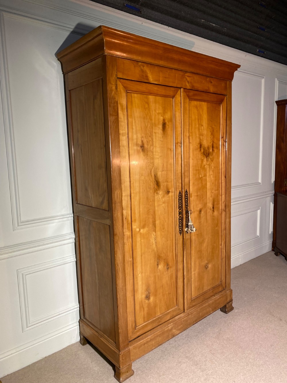 A tall 19th-century cherry wood armoire featuring double panelled doors, decorative iron keyplates, and a projecting upper cornice. View VII