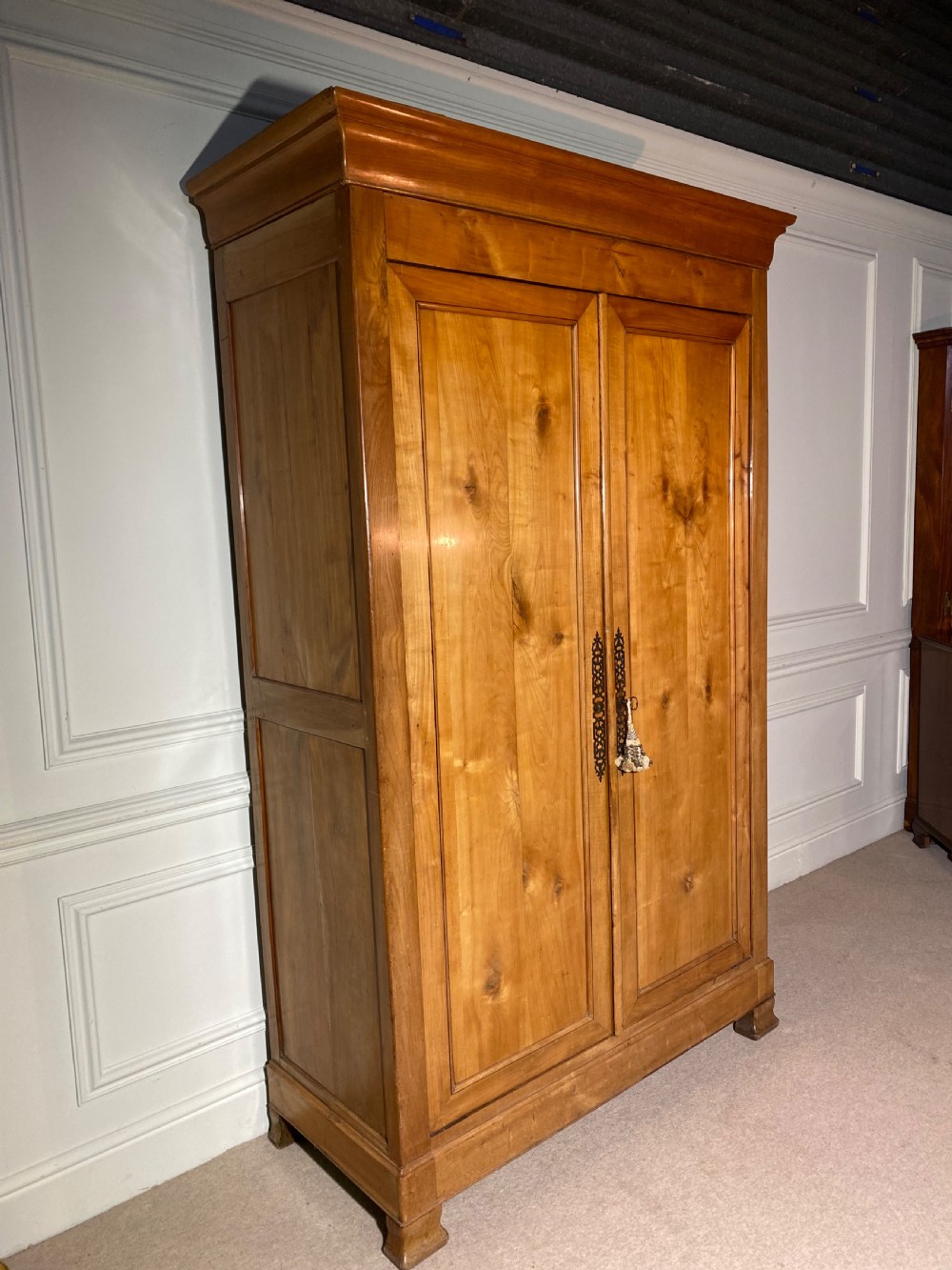 A tall 19th-century cherry wood armoire featuring double panelled doors, decorative iron keyplates, and a projecting upper cornice. View VIII