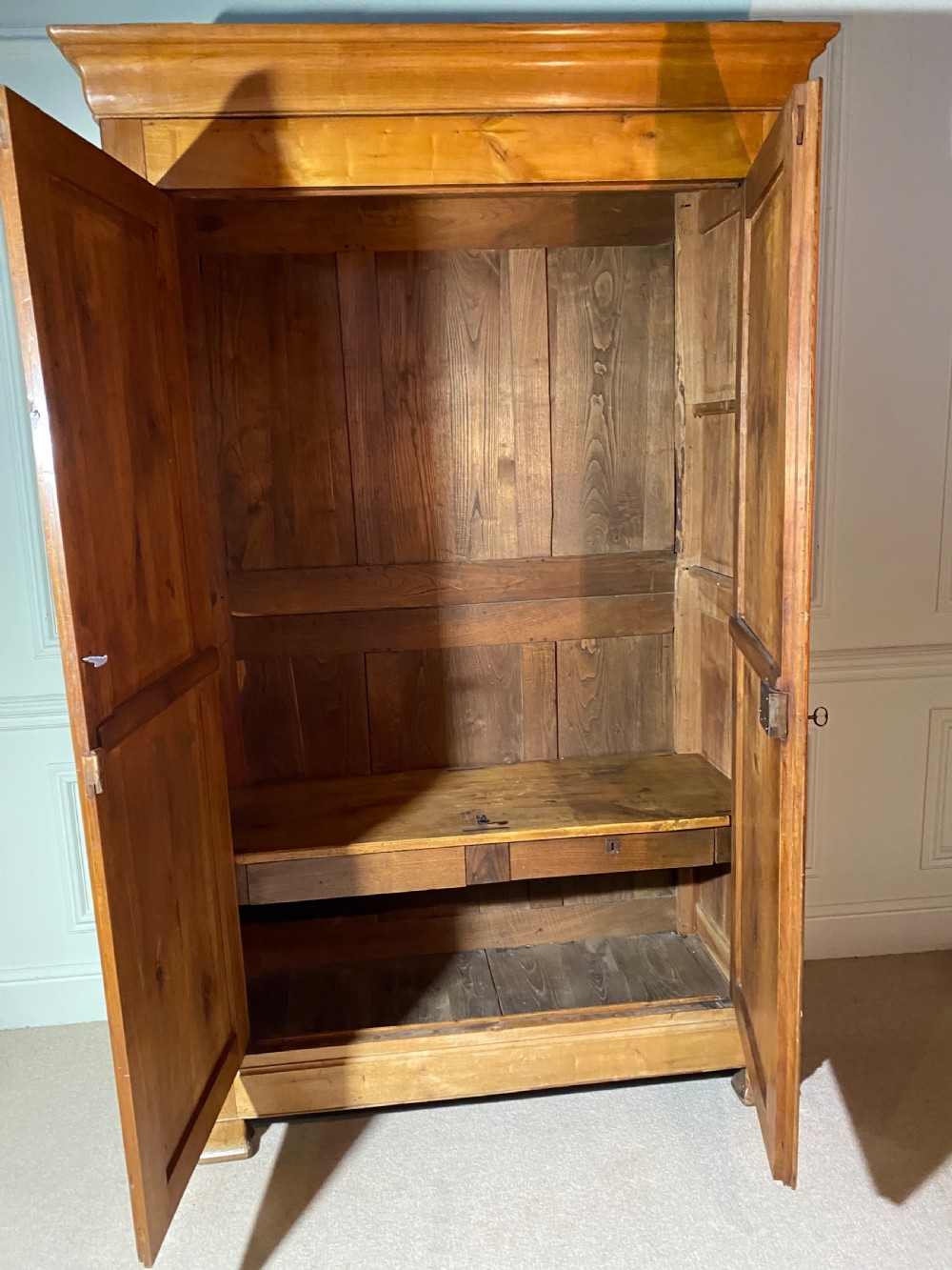 A tall 19th-century cherry wood armoire featuring double panelled doors, decorative iron keyplates, and a projecting upper cornice. View XI