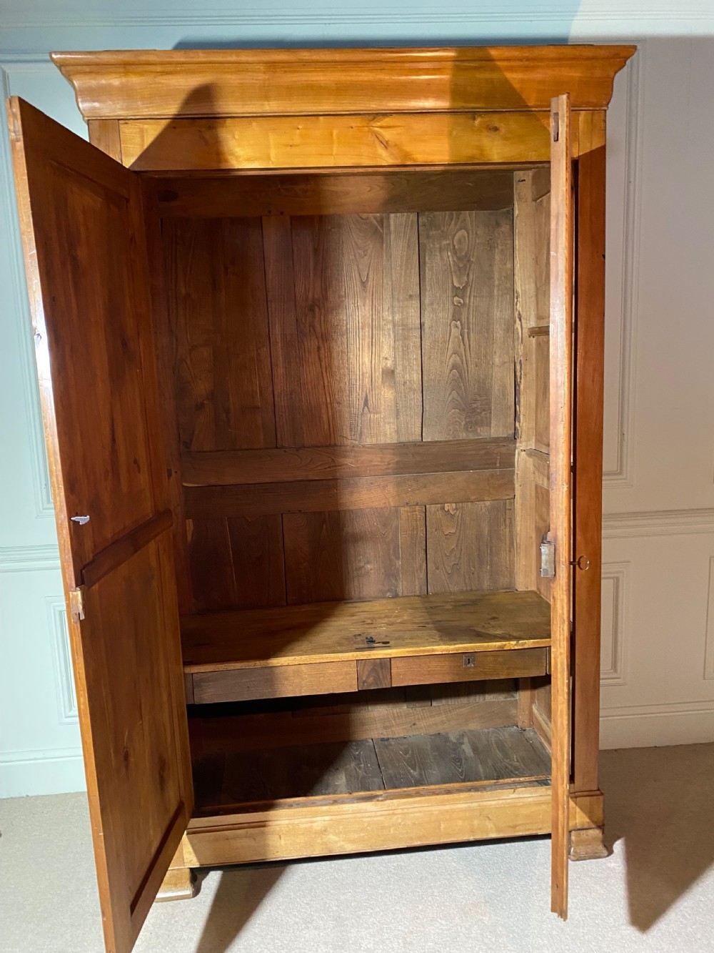 A tall 19th-century cherry wood armoire featuring double panelled doors, decorative iron keyplates, and a projecting upper cornice. View XII