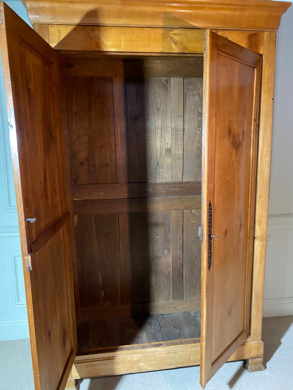 A tall 19th-century cherry wood armoire featuring double panelled doors, decorative iron keyplates, and a projecting upper cornice. View XVII