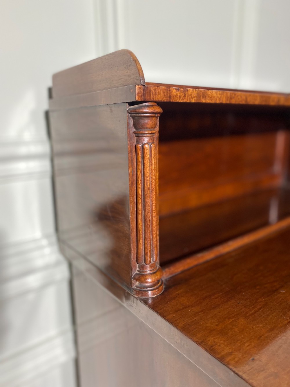 A Regency mahogany chiffonier featuring a raised shelf with reeded column supports above a frieze drawer and a lower cupboard door with brass wire grille and pleated fabric. View X