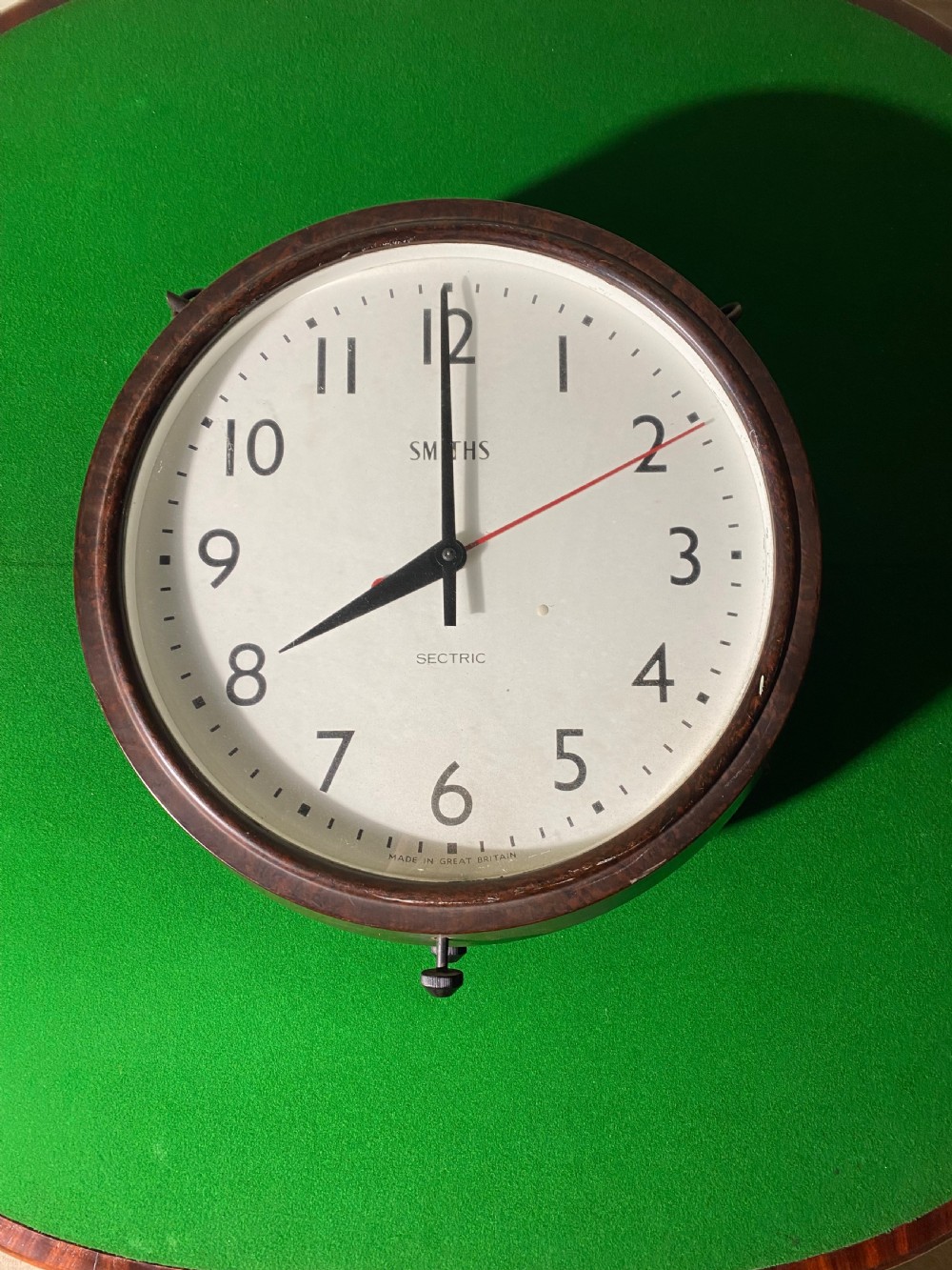 A circular double-sided vintage Smiths Sectric factory clock with a dark brown Bakelite frame and off-white dial face.